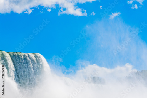 Cascading waters of Niagara Falls set against a vivid blue sky dotted with fluffy white clouds, exemplifying natural majesty at the border of America and Canada. High quality photo