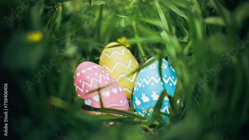Three well hidden bright and vibrant Easter Eggs with intricate carved designs. Focus on Easter Eggs found hidden in dense grass for Easter Egg hunt.