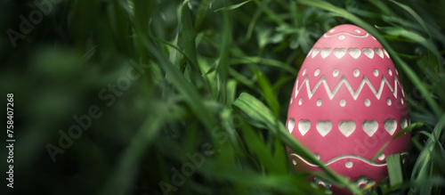 A single well hidden pink Easter Egg with intricate carved design. Focus on Easter Egg found hidden in dense grass for Easter Egg hunt. © Leigh Prather