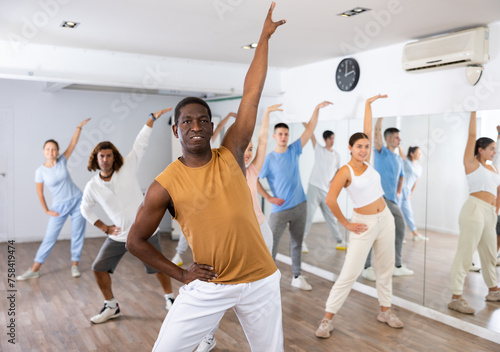 Group of happy young adult multinational sports people exercising dancing in modern gym studio