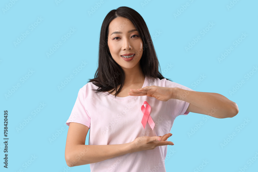 Young Asian woman with pink ribbon on blue background. Breast cancer awareness concept Young Asian woman with pink ribbon on blue background. Breast cancer awareness concept