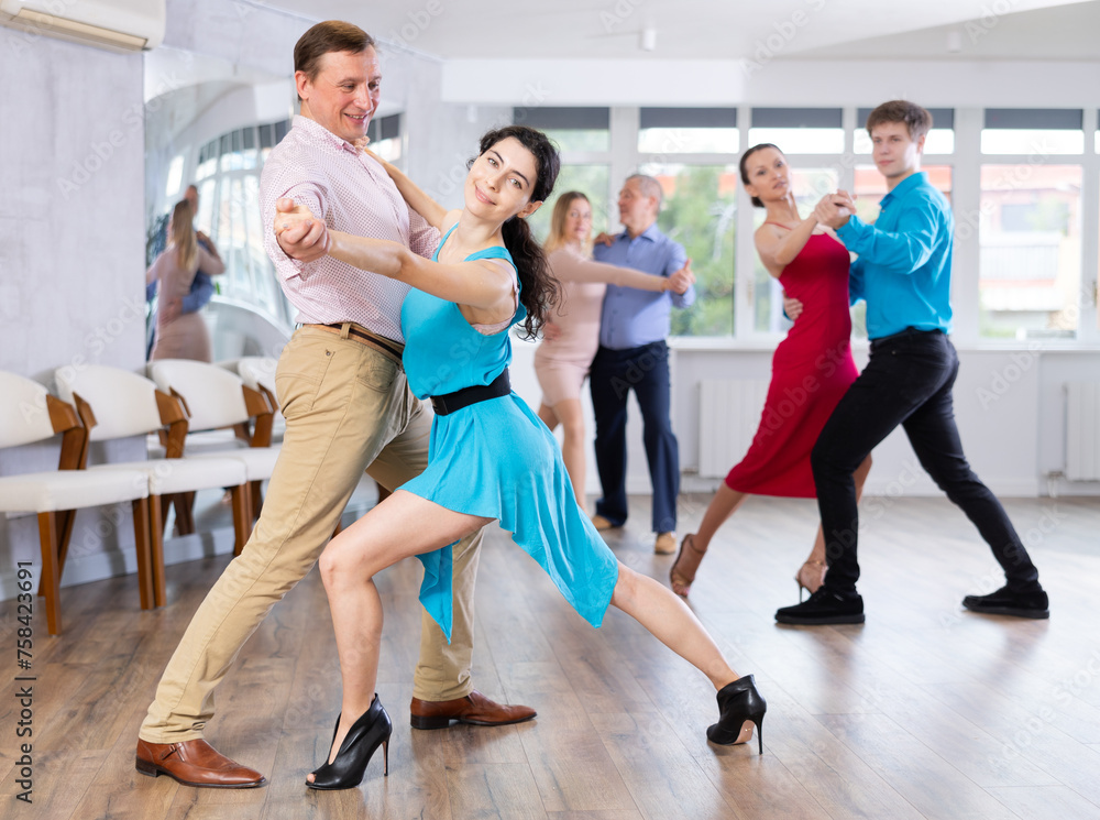 Elegant portrayal of young brunette woman in blue dress, passionately engaged in tango dance with male partner in studio