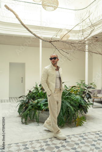 Chico joven tatuado y musculoso posando con ropa contemporánea en el hall de un hotel 