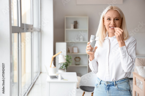 Mature woman with glass of water taking pills at home