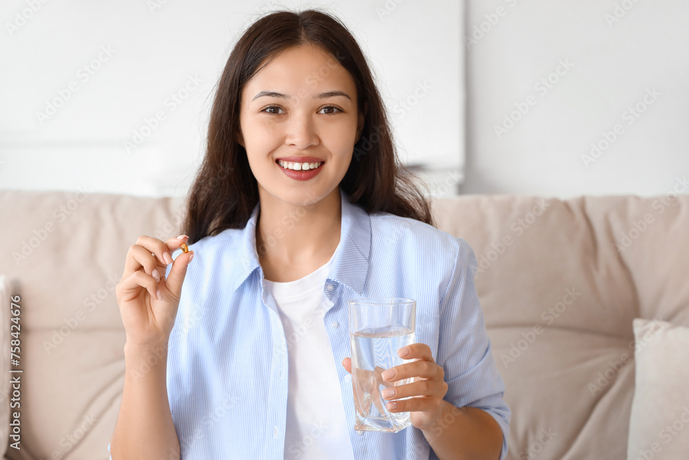 Young Asian woman with glass of water taking pills at home