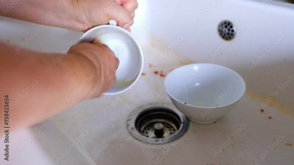 closeup mature female hands washing dirty dishes in white ceramic kitchen sink, using sponge and