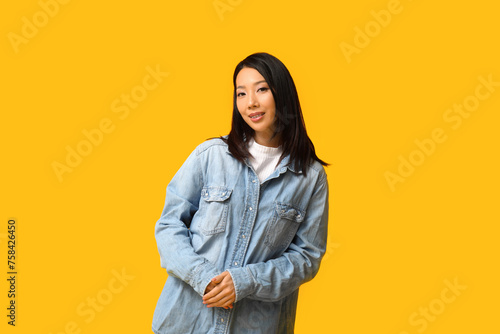 Beautiful young happy Asian woman in stylish denim jacket on yellow background © Pixel-Shot