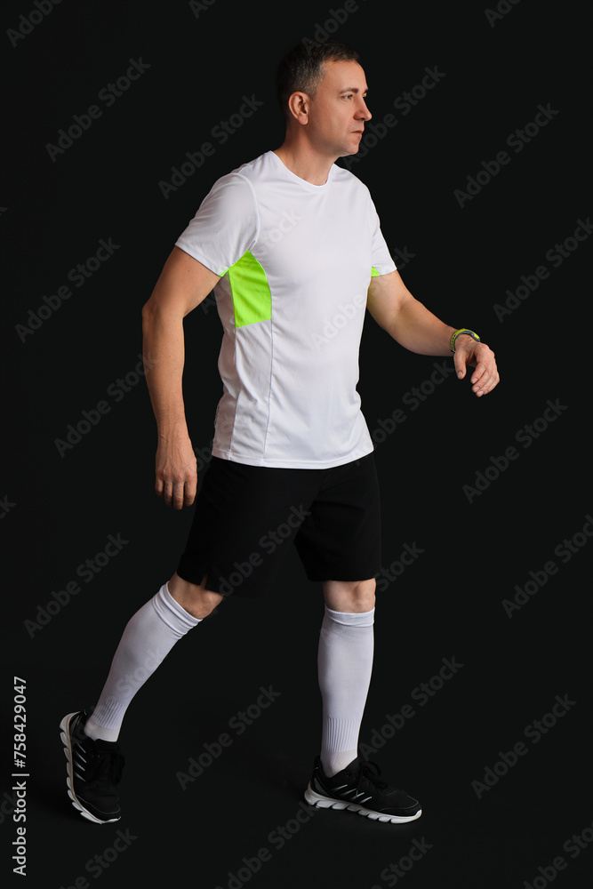 Portrait of sporty middle-aged man walking on black background