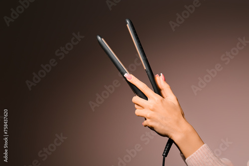 Female hands with hair straightener on pink background, closeup photo