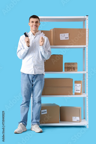 Male online store seller with credit cards and parcel boxes on blue background