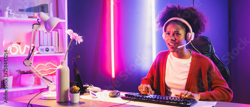 African American girl streamer playing online fighting with Esport skilled team wearing headphones in neon color lighting room. Talking other players planing strategies to win competitors. Tastemaker. © Summit Art Creations