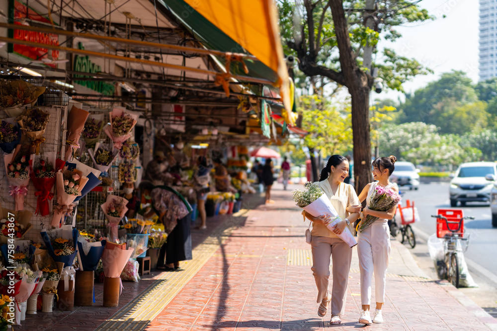 Happy Asian family enjoy outdoor lifestyle travel and shopping together at street market in the city on summer holiday vacation. Mother and daughter holding flower bouquet walking through city street.