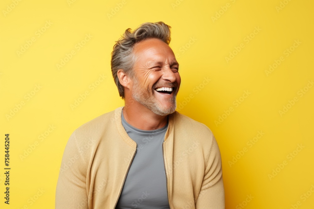 Handsome middle-aged man laughing and looking up on yellow background Handsome middle-aged man laughing and looking up on yellow background