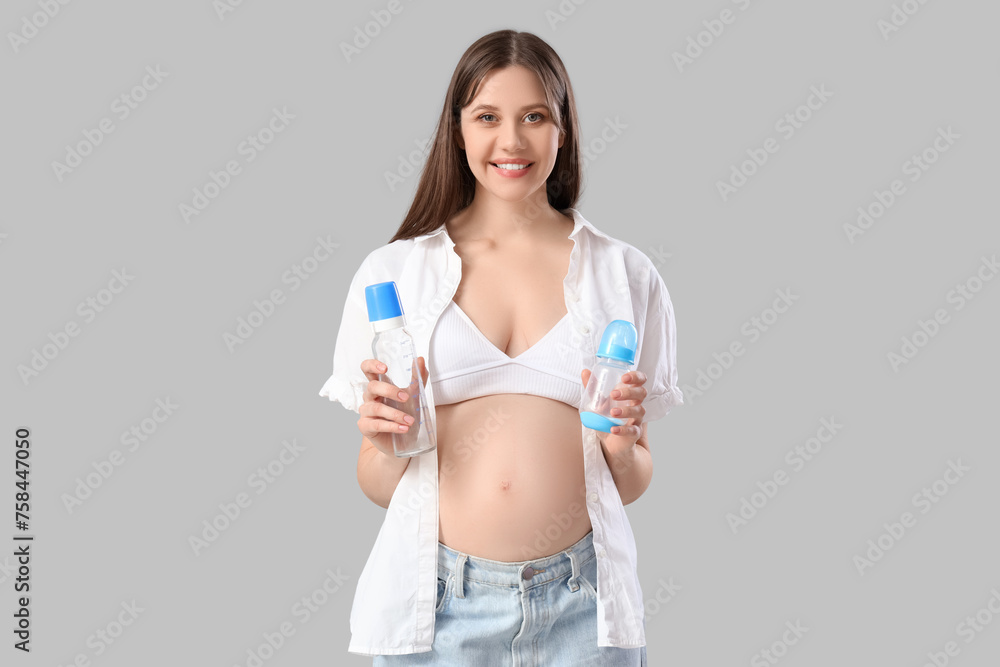 Young pregnant woman with baby bottles on light background Young pregnant woman with baby bottles on light background