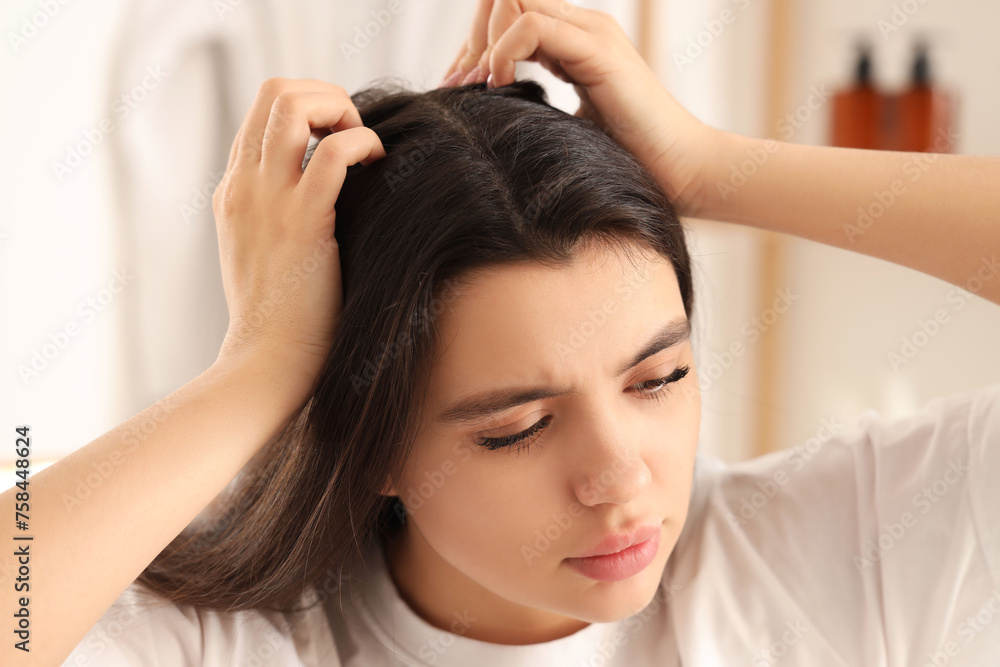 Fototapeta premium Young woman examining her hair for dandruff in light bathroom