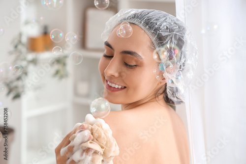 Young woman with loofah and soap bubbles taking bath at home, closeup photo