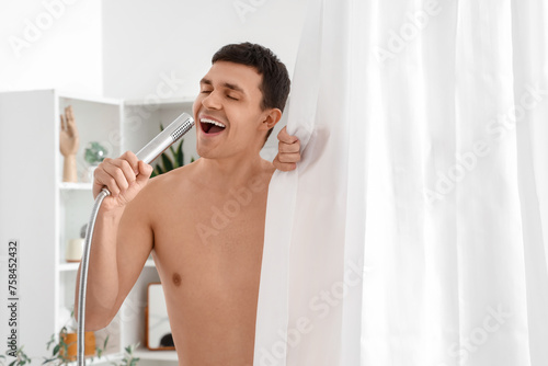 Young man singing with shower head behind curtain in bathroom