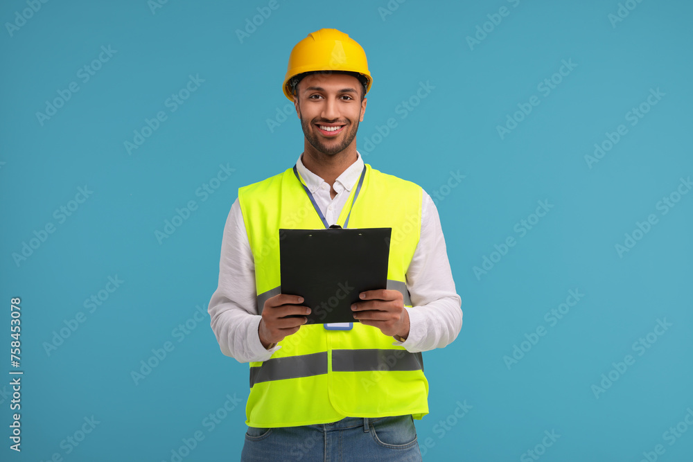 Engineer in hard hat holding clipboard on light blue background Engineer in hard hat holding clipboard on light blue background