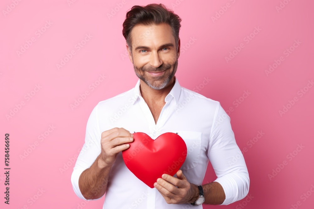 Handsome young man in white shirt holding red heart on pink background Handsome young man in white shirt holding red heart on pink background