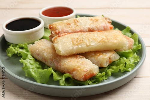 Delicious fried spring rolls and sauces on light wooden table, closeup