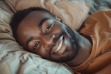 Joyful african Man Lying in Bed. Close-up portrait of smiling man lying in bed, background for bedding store