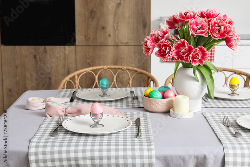 Vase with tulips, Easter eggs and dinnerware on dining table in kitchen