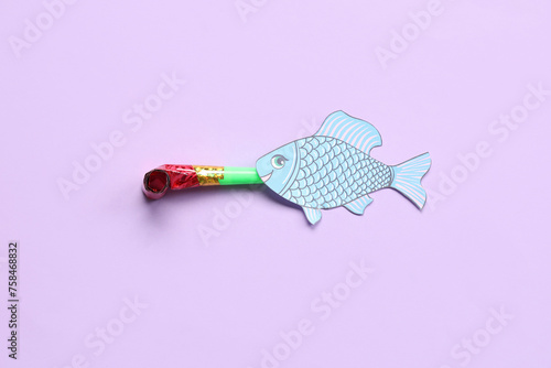 Paper fish with party whistle on lilac background. April Fools Day celebration
