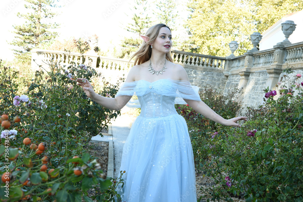 full length portrait of beautiful female model wearing blue fantasy ballgown, like a fairytale princess. walking around a  rose garden in a castle location.