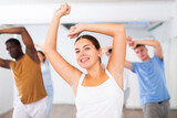 Group of energetic young adult dancers raising both hands up above heads during exercising together in dance hall