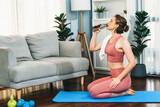 Athletic and sporty woman drinking water on fitness mat after finishing home body workout exercise session for fit physique and healthy sport lifestyle at home. Gaiety home exercise workout training.