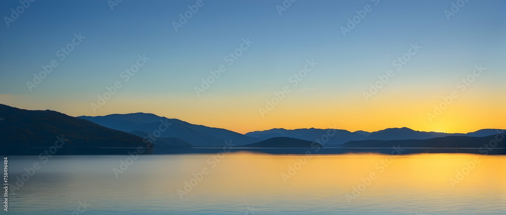 Peaceful coast of the lake with the sun setting, its yellow glow mirrored perfectly on the lake’s surface, under a clear blue sky.