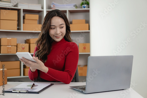 of freelance Asian woman wearing apron using laptop and boxes to receive and review online orders to prepare packs to sell to customers, SME small business entrepreneur, online SME business concept