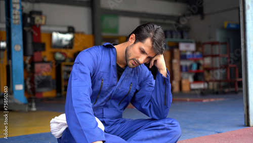 Tired latin auto mechanic bored take a break sitting in garage cars service. Worried hispanic technician repairing auto repair shop . Stress engineer overworked . workers Depressed sad labor burn out photo