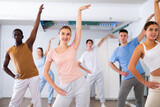 Excited positive diverse men and women of different ages stretching before modern dancing class in school for adults