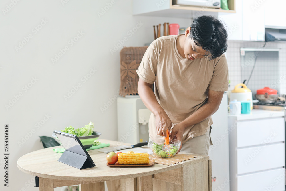 Asian man making salad while watching cooking video tutorial on tablet computer in the kitchen Asian man making salad while watching cooking video tutorial on tablet computer in the kitchen