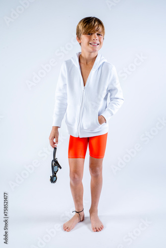Boy youth in swimwear jammers with swim goggles and hoodie standing in studio with white background