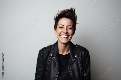 Portrait of a laughing young woman in leather jacket on gray background