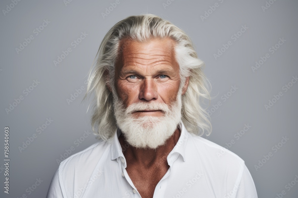 Portrait of senior man with white beard looking at camera while standing against grey background Portrait of senior man with white beard looking at camera while standing against grey background