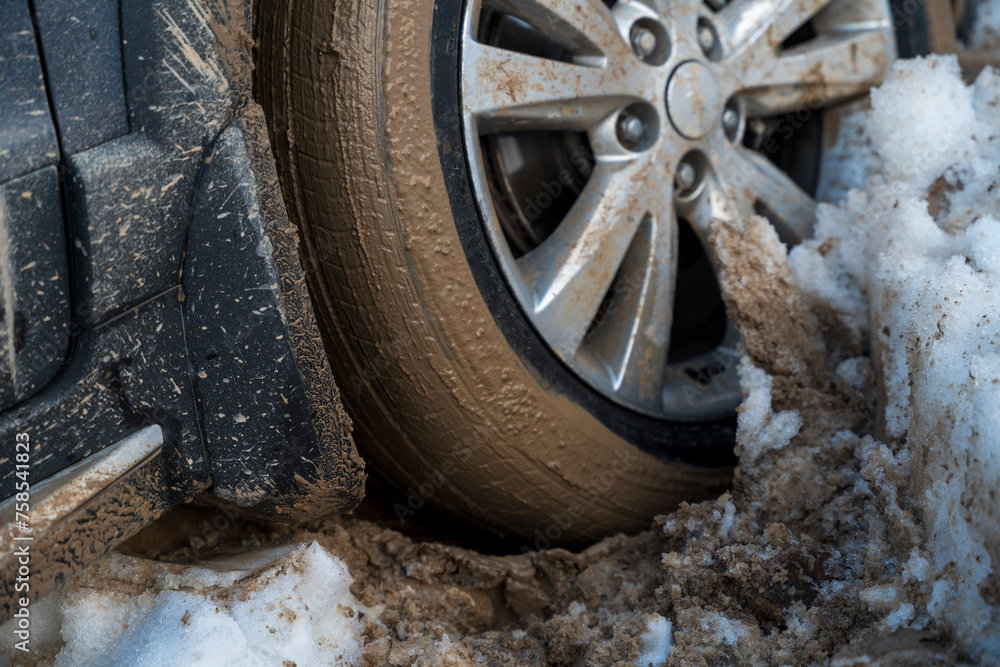 A detailed close-up of a car tire mired in a mix of snow and mud, showcasing the challenges of winter driving. The tread filled with slush emphasizes the need for careful navigation in such conditions A detailed close-up of a car tire mired in a mix of snow and mud, showcasing the challenges of winter driving. The tread filled with slush emphasizes the need for careful navigation in such conditions