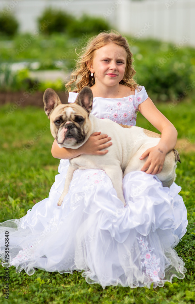 On a hot summer day outside, a beautiful, elegant girl is holding a French bulldog in her arms. A model girl and a dog. On a hot summer day outside, a beautiful, elegant girl is holding a French bulldog in her arms. A model girl and a dog.