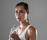 Woman, portrait and fitness with water bottle for hydration, sweat or workout on a gray studio background. Face of female person or athlete with liquid or drink for exercise in health and wellness