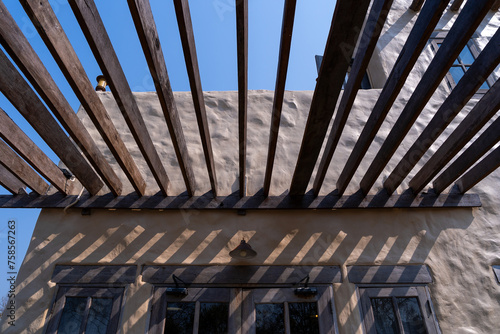 Diagonal shadow lines cast on a textured adobe wall from wooden beams, under a clear sky.