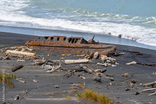 Old wrecked hulk of washed-up boat rusty and surrounded by driftwood in Patea Coastal South Taranaki