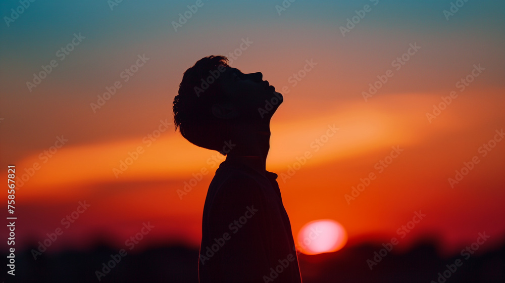 A silhouetted figure gazes up at the setting sun in a dramatic sky. Copy space. Background. Freedom concept.