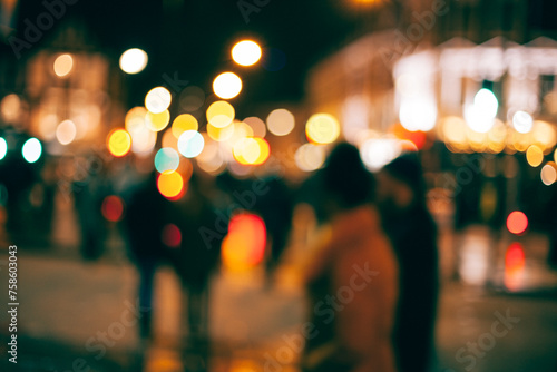 An out-of-focus look at people walking outside in a town at night with with blurs of dotted light all around. photo