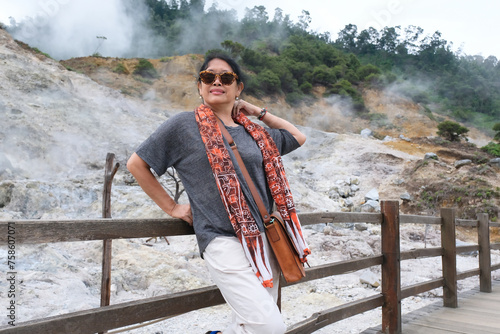 Woman stopping over smokey volcanic crater after walking along wooden bridge photo