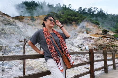 Woman posing over smokey volcanic crater after walking along wooden bridge at Sikidang volcanic crater photo