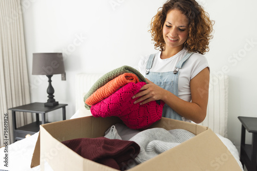 A young Caucasian woman unpacks colorful sweaters from a box and sorts clothes for donation photo