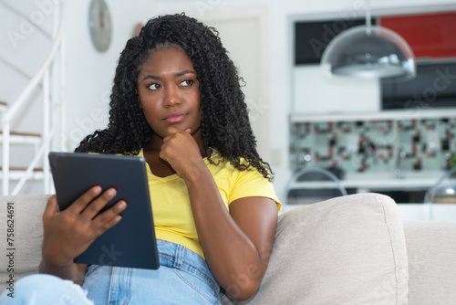 Thinking corpluent african american female young adult with tablet computer