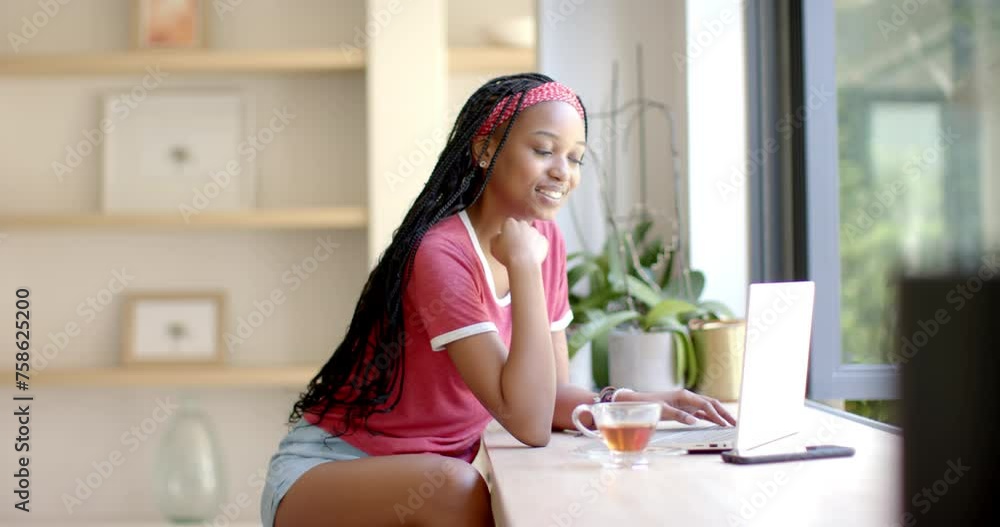 A young African American woman is working on her laptop in the kitchen A young African American woman is working on her laptop in the kitchen